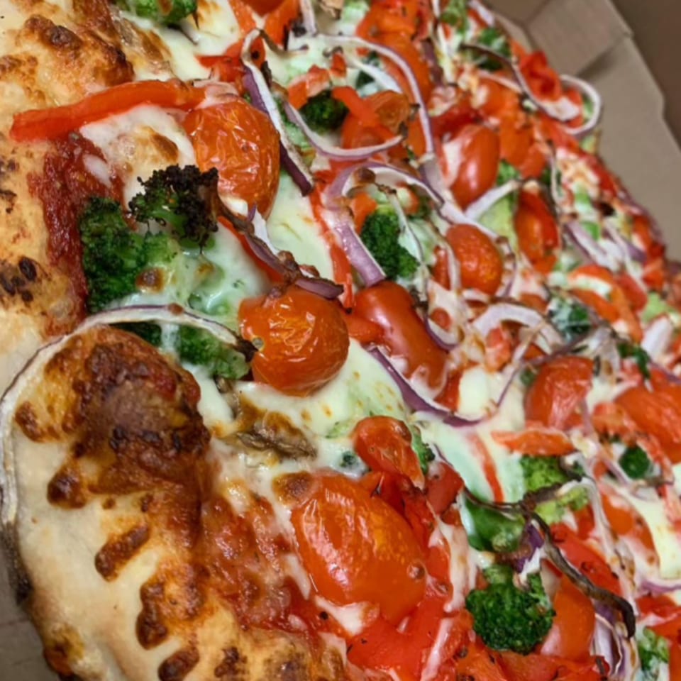 Close-up of a Mamma Mineo's pizza with melted cheese, red tomatoes, broccoli, and red onions.
