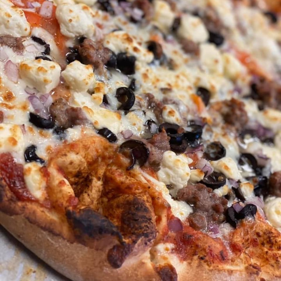 Close-up of a Mamma Mineo's pizza with sausage, black olives, red onion, and ricotta cheese.