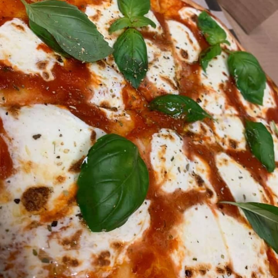 Close-up of a Mamma Mineo's pizza with melted mozzarella, red sauce, and fresh basil leaves.
