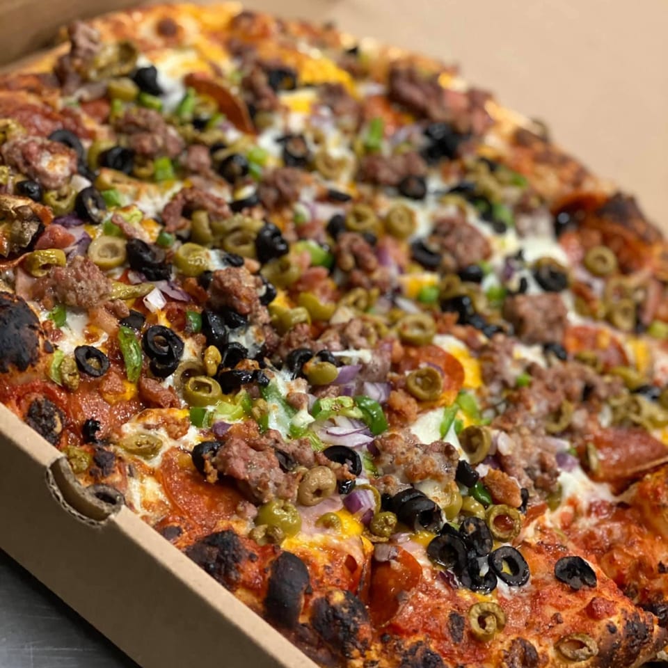 Close-up of a Mamma Mineo's pizza with pepperoni, sausage, green peppers, onions, and olives.